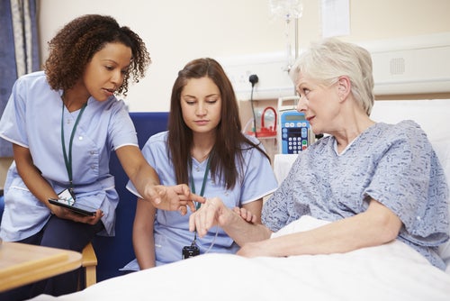 A nurse educator shows a student nurse how to assess symptoms presenting on a patient’s wrist.